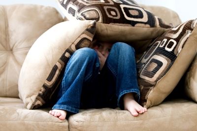 kid hiding under pillows on sofa